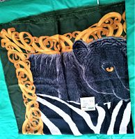 Close-up of corner of scarf showing black panther and zebra stripes with gold swirl border detail on green fabric base