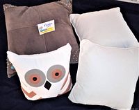 Lot of 4 vintage couch pillows including brown suede-like pillow with studs, owl face pillow, and two plain white pillows against dark background.