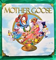 Front cover of the 2002 Keepsake Collection Mother Goose book showing colorful illustrations of nursery rhyme characters including Mother Goose herself surrounded by children and animals, with gold foil title and corner accents, laid on green fabric surface.