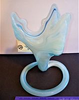 Blue and white swirled glass tulip vase on round base viewed from the side showing the unique curled top opening and swirl pattern.