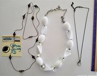 Overview of three necklaces: black bead cluster necklace, chunky white bead necklace, black chain with clear rectangular pendant.