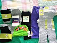 Photo showing black and gray baby leggings, Teenage Mutant Ninja Turtles green cap hat with tags, and purple clothing items.