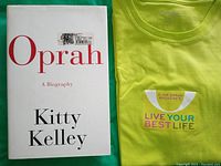 Hardcover biography book titled 'Oprah' by Kitty Kelley and a folded bright yellow T-shirt with slogan and branding visible.