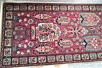 Top down view of rectangular red Anglo-Persian patterned rug with floral and geometric motifs bordered by intricate designs.