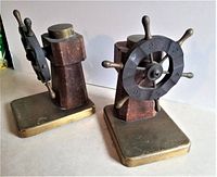 Pair of vintage brass, wood, and Bakelite ship wheel bookends showing front and side views. The wheels have turning mechanisms with numbers 1 to 6. One wheel has two missing handles.