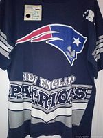 Front view of vintage blue New England Patriots shirt showing large team logo and text with stripe sleeve detail.