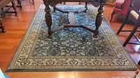 Full view of rectangular polyester area rug under a table, showing blue floral pattern with beige border.