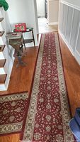 Long carpet runner laid in a hallway showing full length with red and beige floral design and beige border.