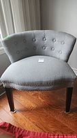 Front view of the vintage parlor chair showing the rounded back, button tufting, nailhead trim, and dark wooden legs with metal protectors.