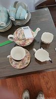 Floral teapot with matching teacup, saucer, sugar dish and creamer on wooden table.
