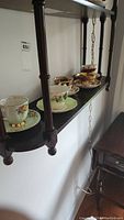 Five sets of teacups and saucers displayed on a dark wooden wall shelf, showing various floral patterns and gold accents.