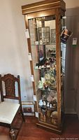 Full front view of tall oak wood display case showing glass door with multiple shelves inside and some decorative items, none included in lot.