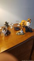 Overview of all eight figurines including five dogs, two glass birds and snowman on a wooden surface.