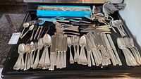 Wide overview of the full flatware collection showing various knives, forks, spoons and specialty pieces laid out on a stove top.