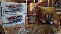 Photo showing two boxed Hot Stone Grills sets, one 8-piece fondue set box, and a dessert fondue pot on glass table.