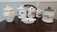 View of full set of six ceramic food containers with various floral and fruit designs on a wood table.