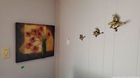 Wall arrangement with three gold metal geese sculptures in flight and a floral canvas in background.