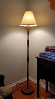 Full view of the mid-century modern wooden floor lamp illuminated in a corner beside furniture and books.