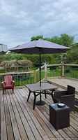 Full view of patio setup showing metal table with umbrella and base on wooden deck, mood cloudy weather.