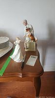 Two Royal Doulton porcelain figurines on a wooden table. The man and dog figurine is titled "Thanks Doc" and the woman reading a note is titled "Thank You".
