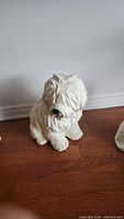 Front view of the large white ceramic shaggy dog figurine sitting on a wooden floor.