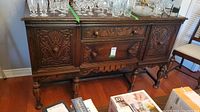 Front view of the vintage wooden sideboard showing detailed carved floral patterns, central drawers, and cabinet doors with carved handles.