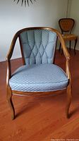 Front view of vintage armchair with blue patterned cushioned seat and button-tufted back, wooden curved arms and legs visible.
