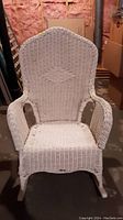 Front view of vintage white wicker rocking chair showing high back with diamond pattern, armrests, and rocking legs.