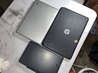 Three laptops closed on table - two HP (silver and black) and one RCA (black)