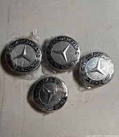 Four Mercedes-Benz blue factory OEM wheel center hubcaps arranged on a flat surface, showing front view with star logo and branding.