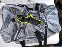 Top and side view of gray duffel bag with neon yellow-green zipper and black straps on white surface.