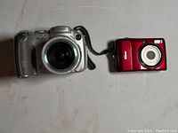 Front view of Canon PowerShot S2 IS and Nikon Coolpix L20 cameras placed side by side, showing lens and body details.