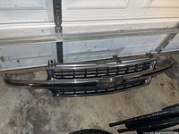 Front grille for Chevy Silverado 1500/2500 trucks shown from front side on a concrete floor with visible chrome and black plastic components.