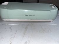 Front view of a mint green Cricut Explore Air 2 with closed lid on a stained white table