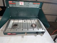 Green Coleman Classic propane stove with two burners and wind guards, shown from top angle