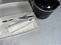 White Proctor Silex handheld electric mixer with two beaters in white plastic case, white power cord coiled.