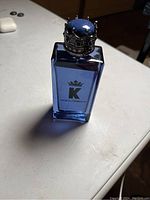 Front view of Dolce & Gabbana K cologne bottle, showing the blue glass and crown cap with decorative details.