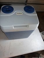 Top angled view of Ivation cooler showing dual blue fans and Ivation logo on white top and blue cooler base.