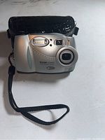 Front view of Kodak DX3600 Zoom digital camera showing lens and wrist strap with carrying case behind