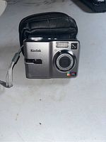 Front view of Kodak Easyshare C743 digital camera with lens and flash, wrist strap visible, placed in front of black carrying case.