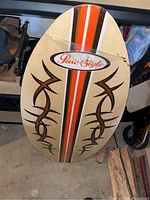 Top view of the Pure Style surfboard showing the tribal designs and the orange-white-black racing stripes with a center logo, sealed in plastic.