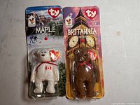 Photo showing two rare TY McDonald's Teenie Beanie Babies in original sealed packaging: Maple the Bear and Britannia the Bear, each mounted on themed backing cards representing Canada and the UK respectively.