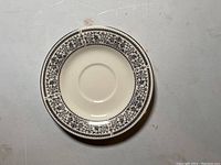 Top view of one ivory porcelain plate with brown floral and geometric Georgian pattern around rim.