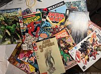 Top view of a spread of 16 comic books stacked visibly, showing various superhero and graphic novel covers.