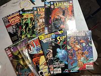 Stack of 10 assorted comic books on table displaying cover artwork and titles including Kamandi, The Avengers, Superman, Justice League and more.