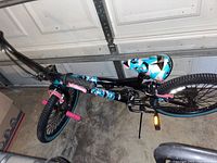 Photo showing one BMX bike lying on its side with geometric patterned saddle, pink pedal pegs, black and teal rims, black frame.