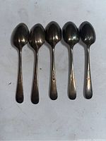Five vintage Elkington silver plated spoons laid out in a row, showing their front side and identifying marks on handle