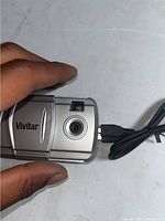 Front view of a silver Vivitar digital camera showing the lens, viewfinder, and USB cable attached.