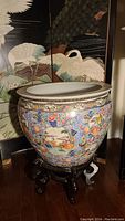 Full view of large colorful Asian fishbowl on carved wooden stand showing exterior design and proportions
