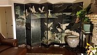 Full view of the 8-panel Asian screen displaying carved and painted cranes by the ocean scene with mountains behind, positioned in a living room.